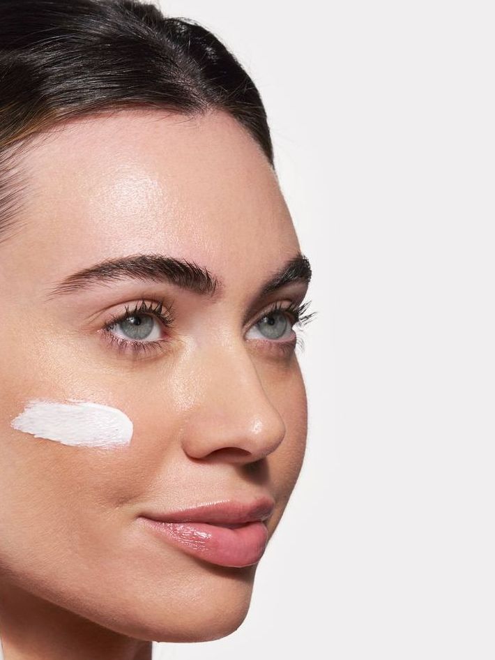 Woman with fair skin, a swipe of white cream on her cheek.