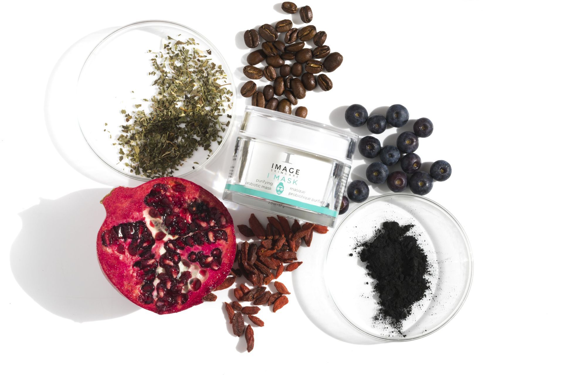 Ingredients and cosmetic cream jar; pomegranate, coffee beans, blueberries, goji berries, herbs, charcoal.