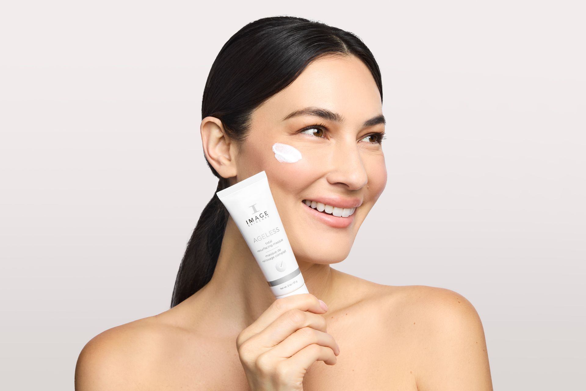 Smiling woman holding skincare tube, cream on cheek.