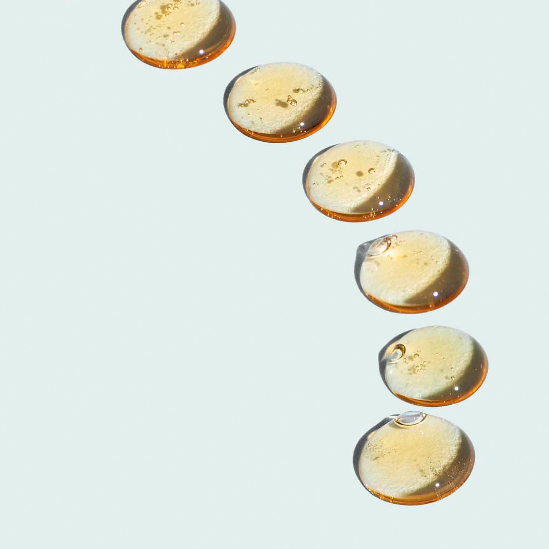 Six amber liquid droplets descending on a light blue background.