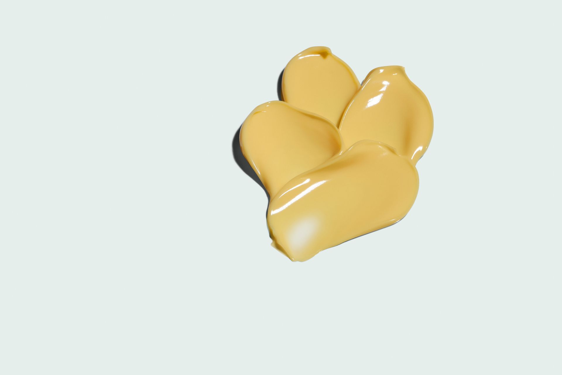 Swatches of yellow-toned foundation on a light blue background, showing texture and highlights.