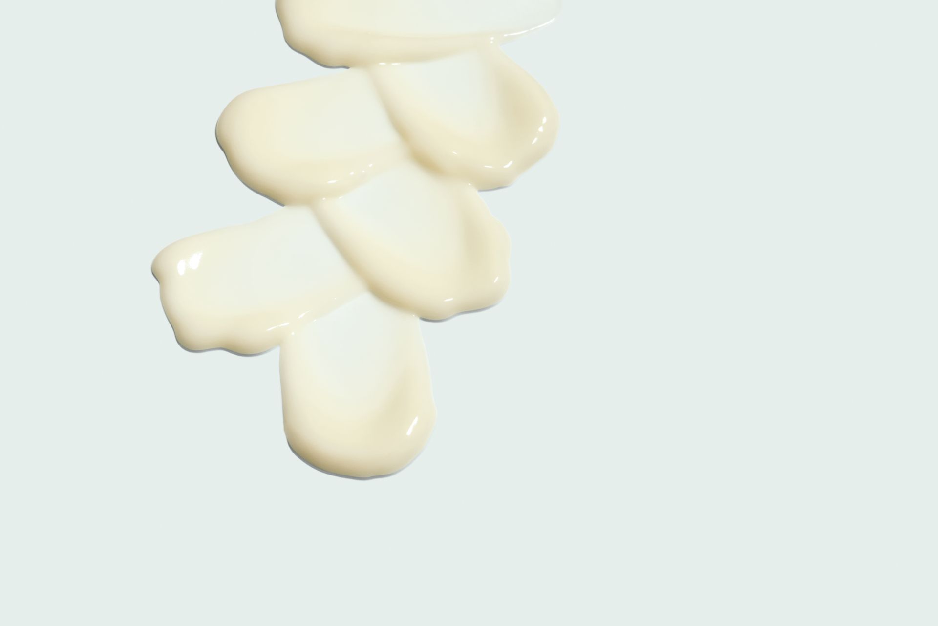 Swatches of creamy, light-yellow cosmetic product arranged like a flower on a light blue background.