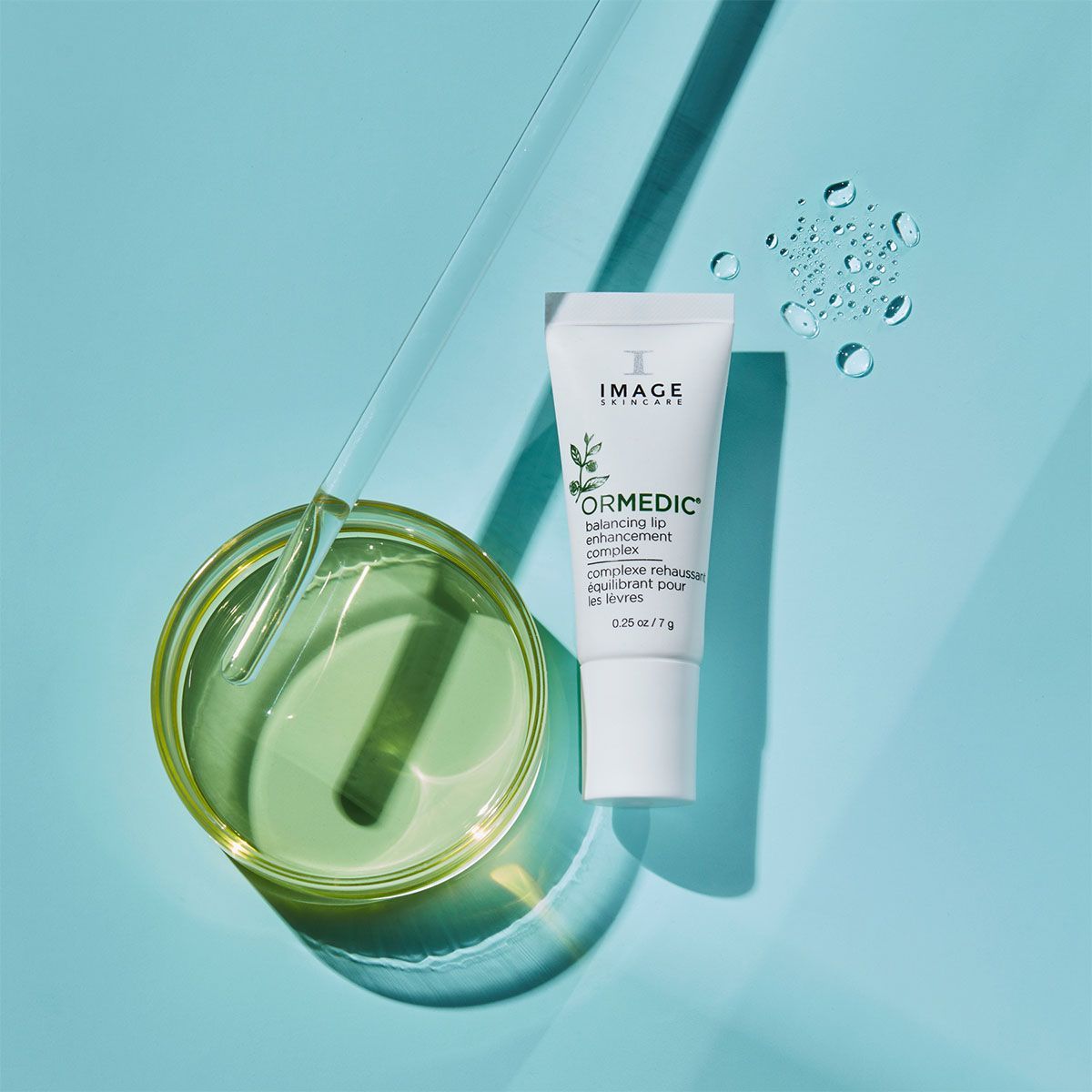 White tube of Ormedic skincare product next to a petri dish and water droplets on a blue surface.