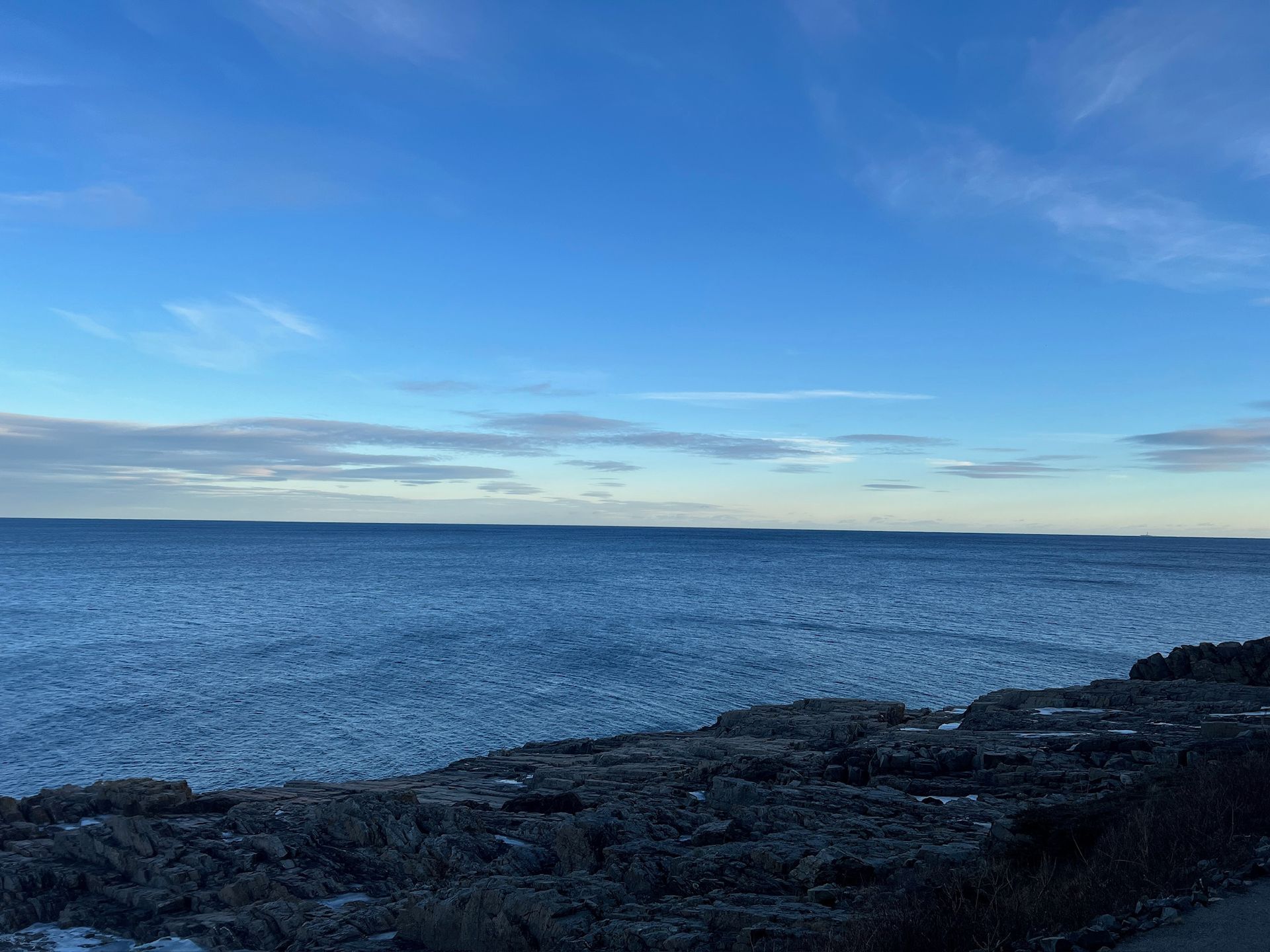 The coast of Maine, outside the Cliff House. Rugged cliffs meet up to the vast blue ocean, which extends into the blue sky.