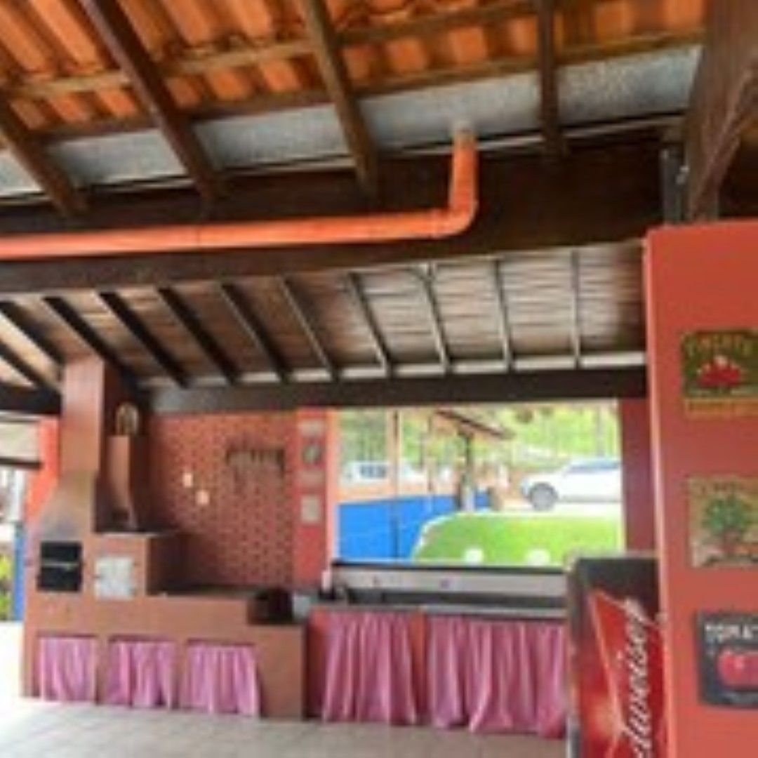 Cozinha ao ar livre com forno de tijolos, detalhes em vermelho e rosa, teto de madeira e vista verde.