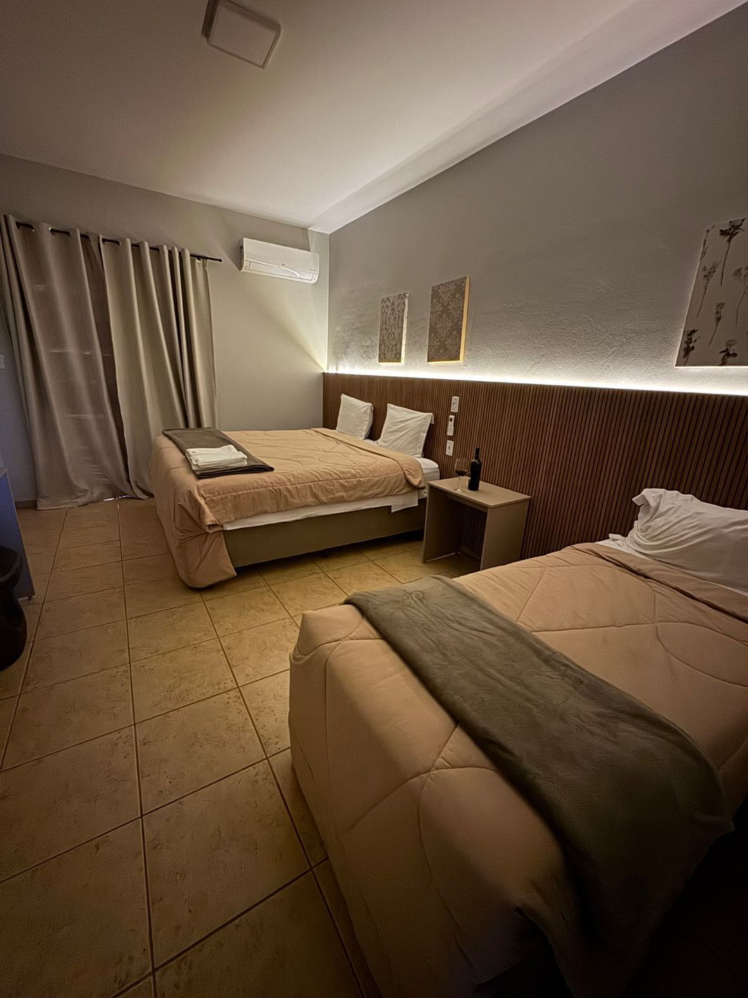 Quarto com duas camas: uma de casal e uma de solteiro. Roupa de cama bege, piso bege, paredes cinza.