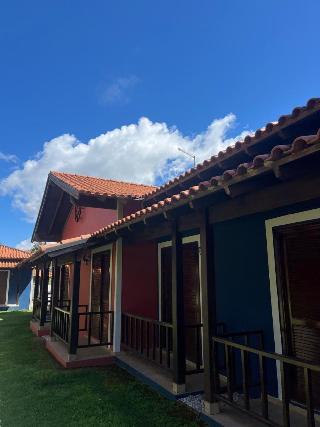 Fileira de chalés coloridos com paredes vermelhas e azuis, detalhes marrons e telhados vermelhos sob um céu azul.