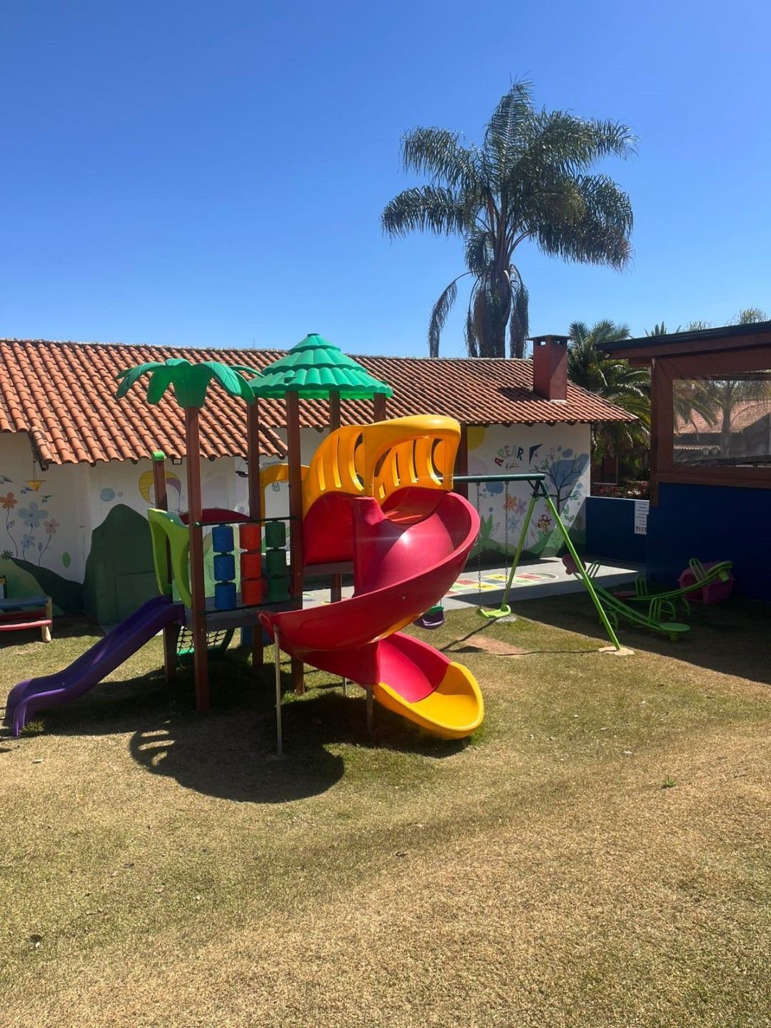 Parque infantil com escorregadores coloridos e um prédio em um quintal gramado.