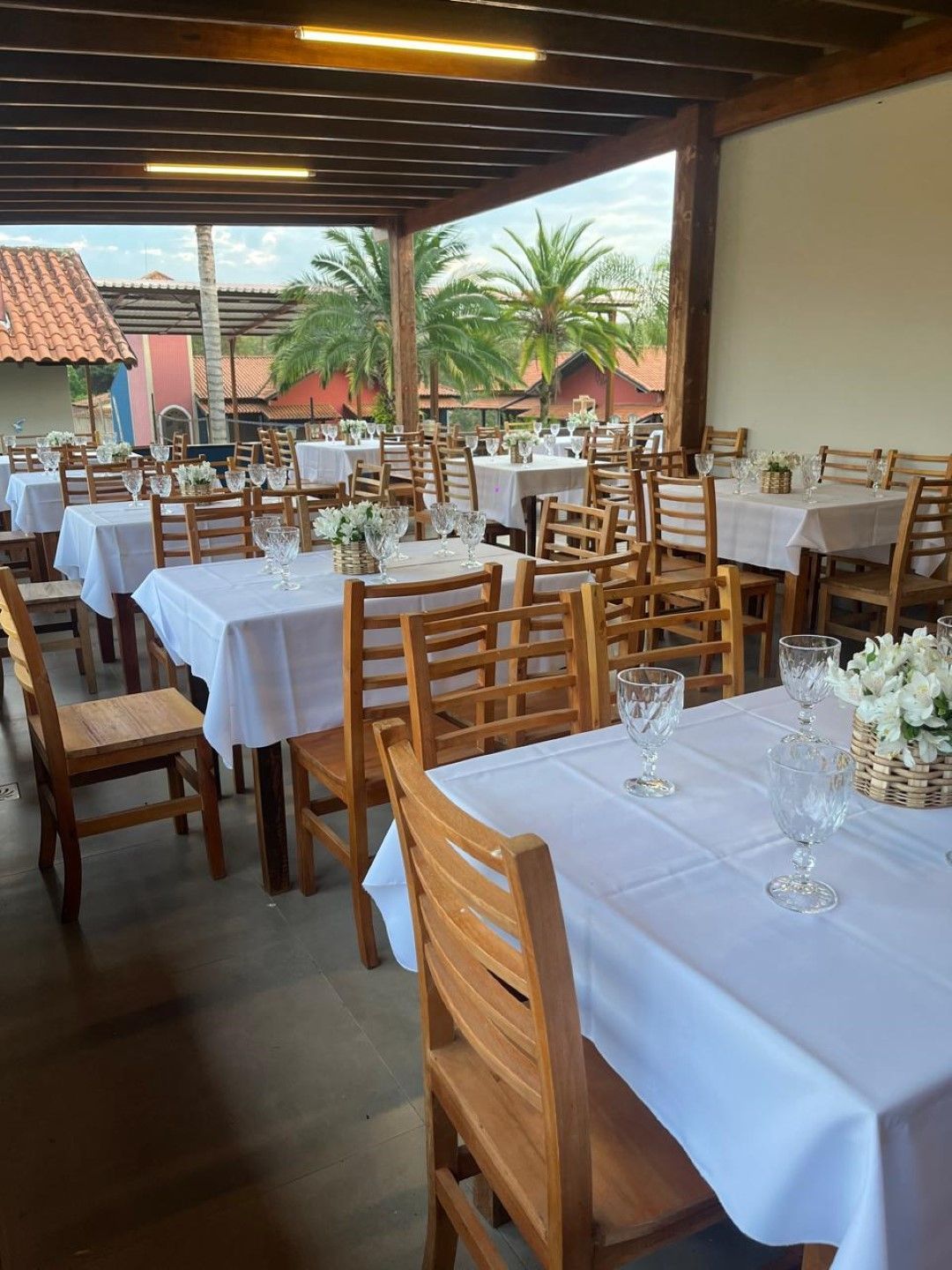 Área de jantar do restaurante com toalhas de mesa brancas, cadeiras de madeira e arranjos florais.