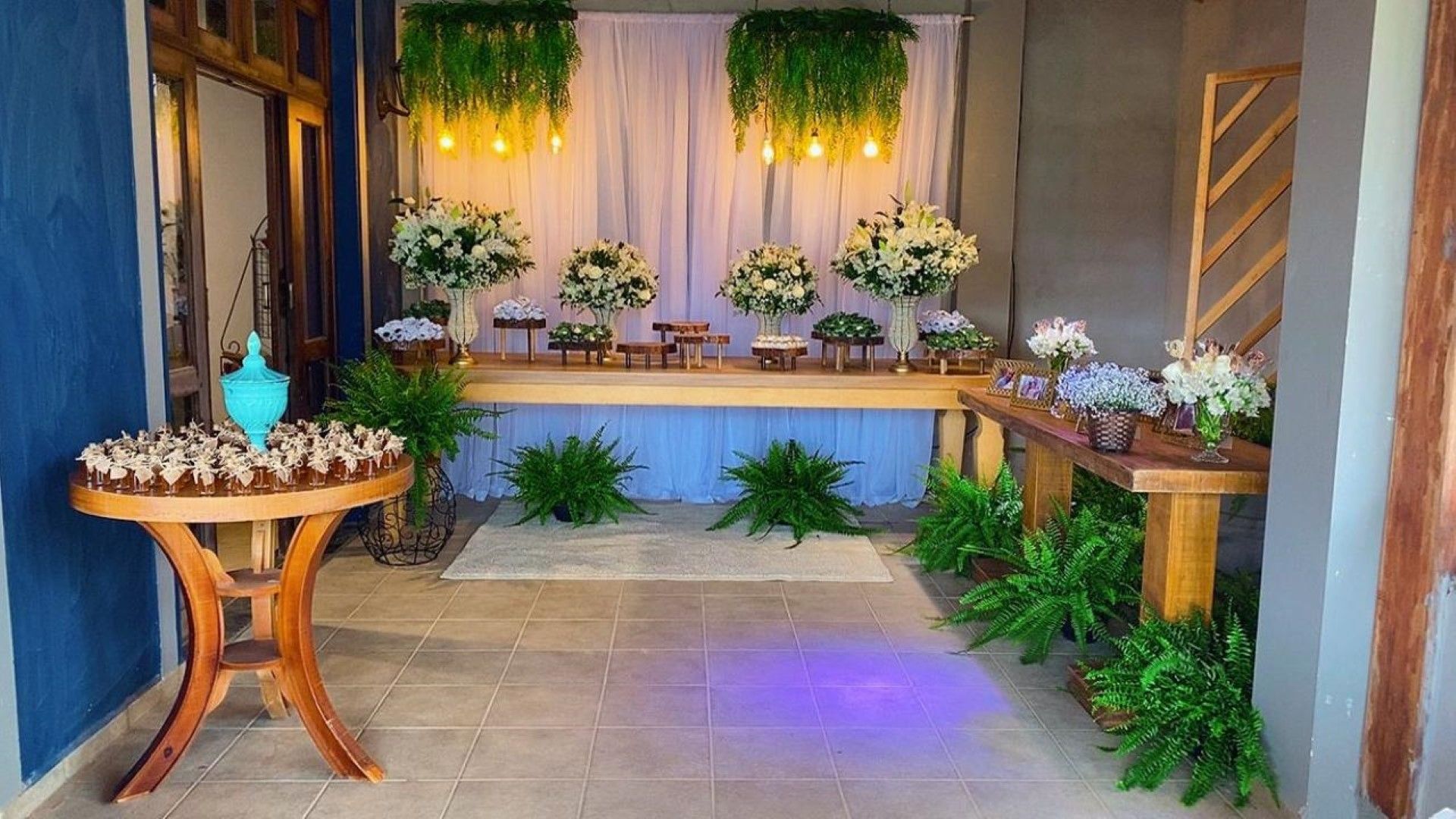 Mesa de sobremesas de casamento com flores e luzes penduradas.