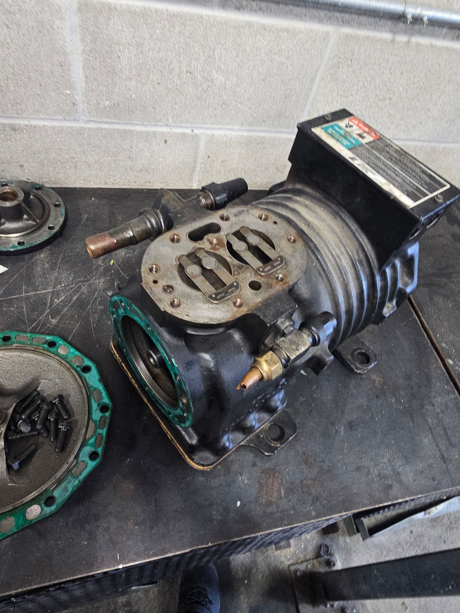 Black air compressor disassembled on a metal surface, showing internal components.