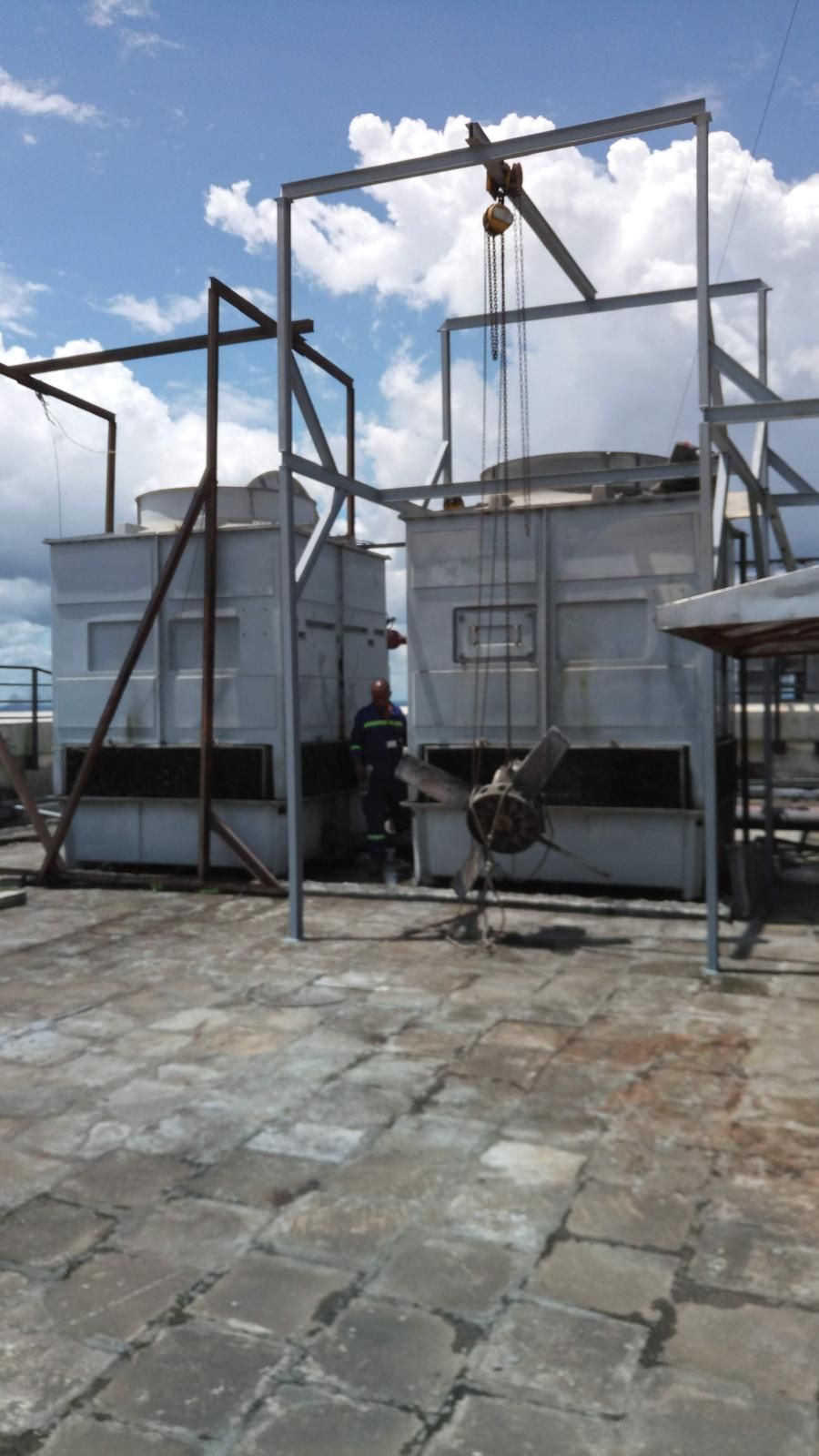 Cooling towers on a rooftop. Workers stand near the machinery under a blue sky.
