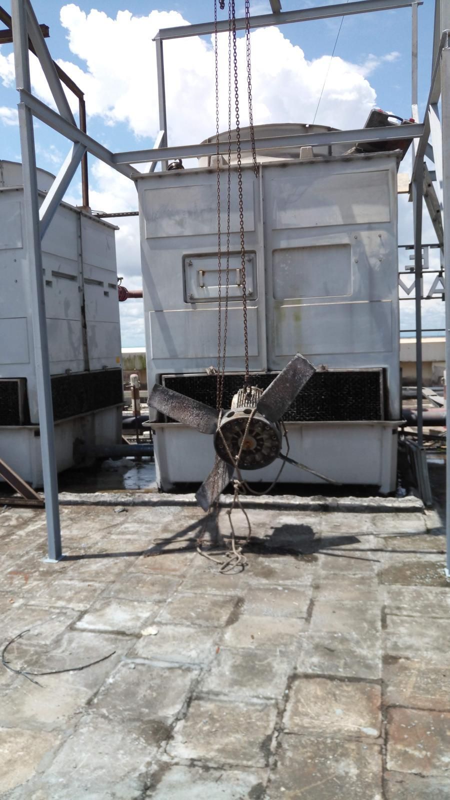 Cooling towers on a rooftop. Gray metal structures with a fan in the foreground and a cloudy sky.
