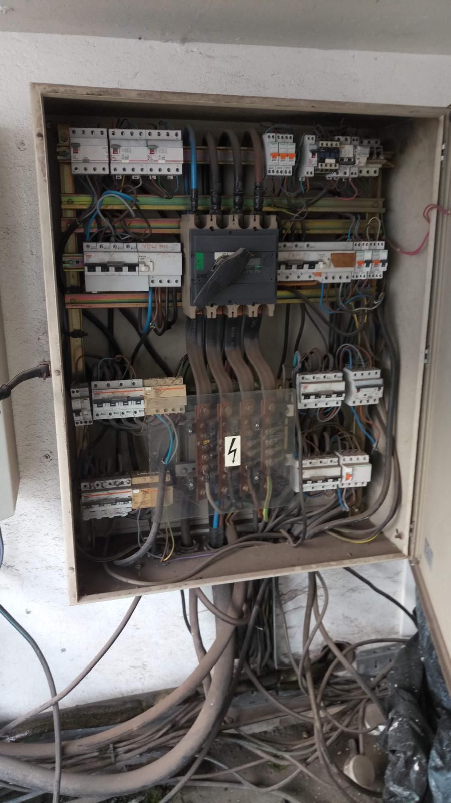 Electrical panel with various circuit breakers, wires, and a main switch, mounted inside a metal box.