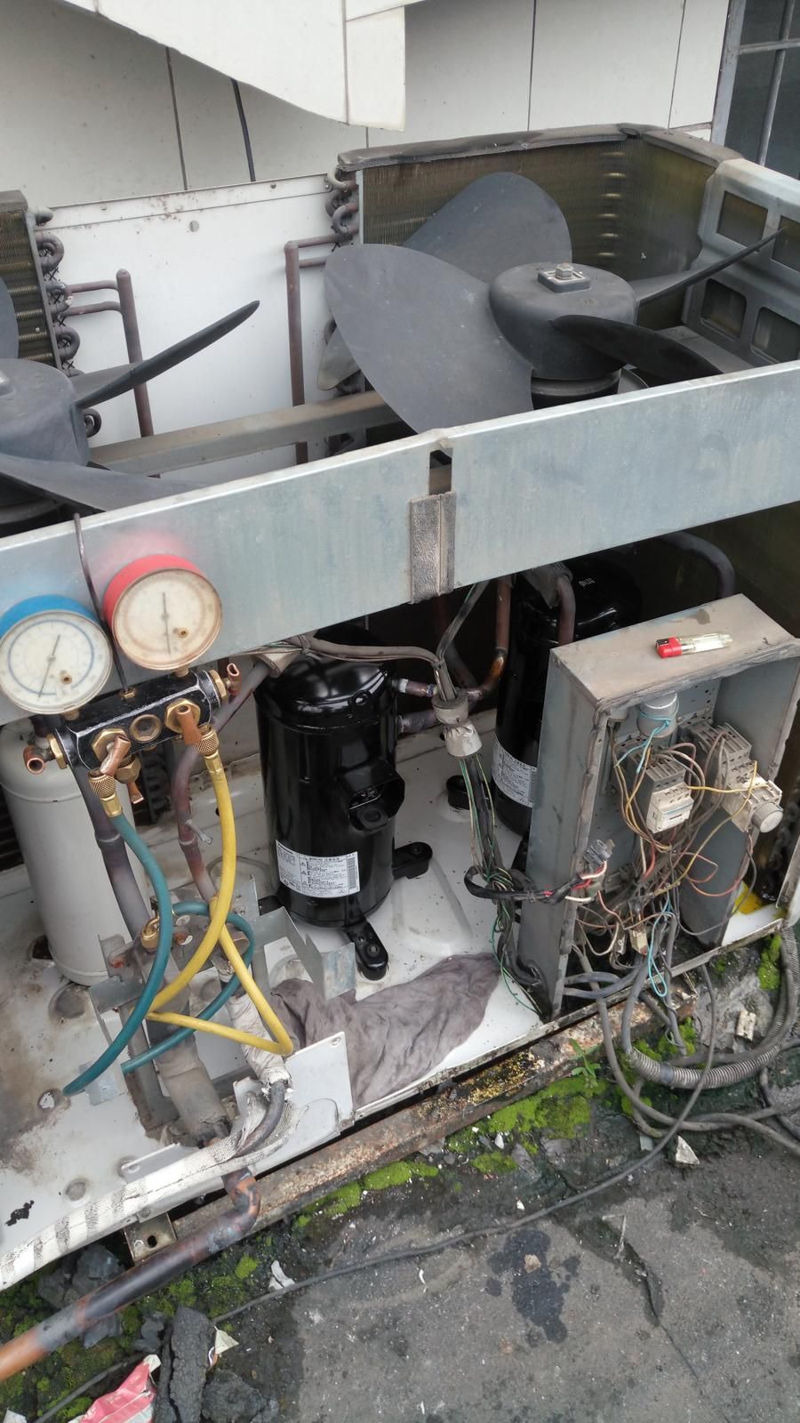 Opened air conditioning unit showing components, gauges, compressor, and fan. Metal casing, wires, and tubes visible.