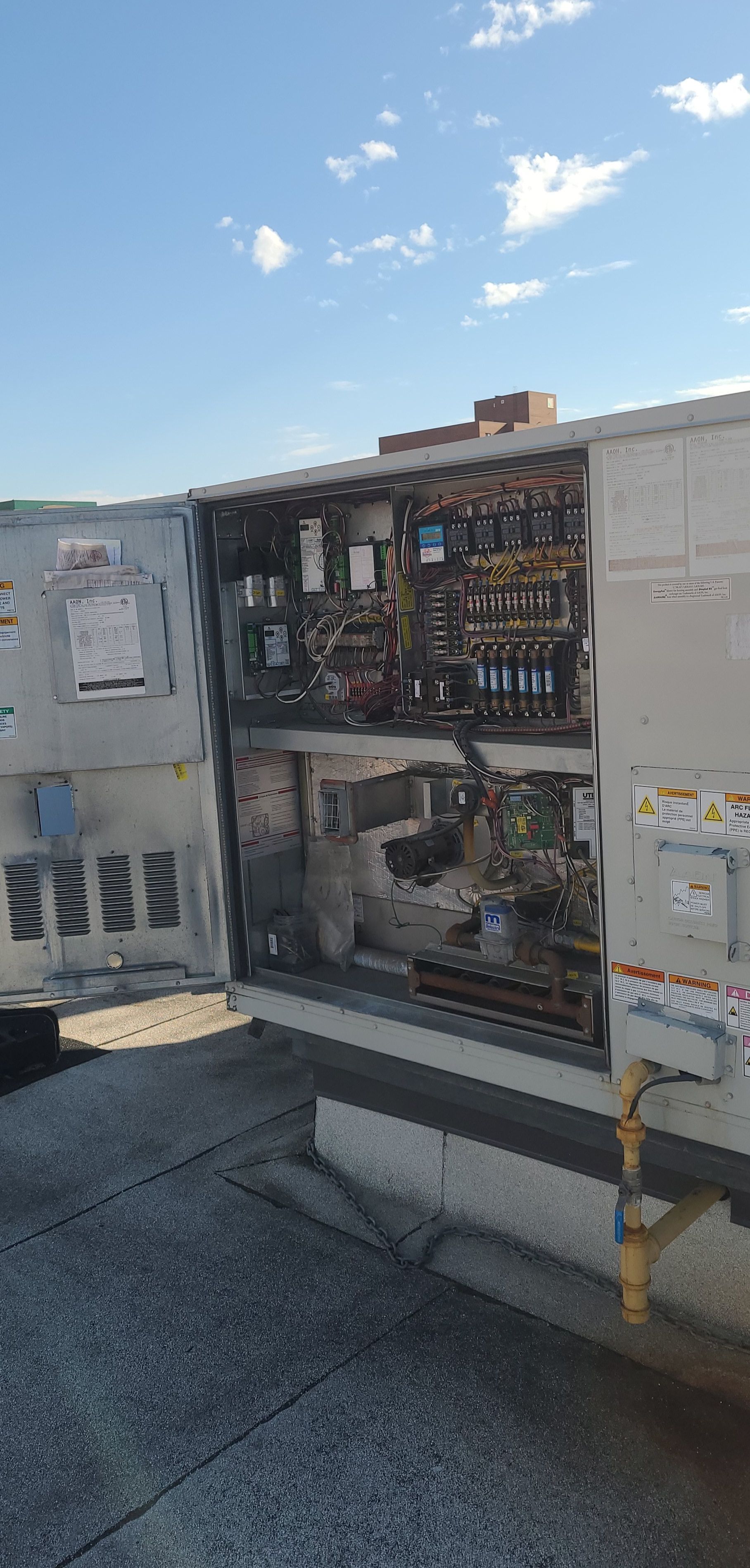 Open electrical panel on a rooftop against a blue sky, revealing interior components and wiring.