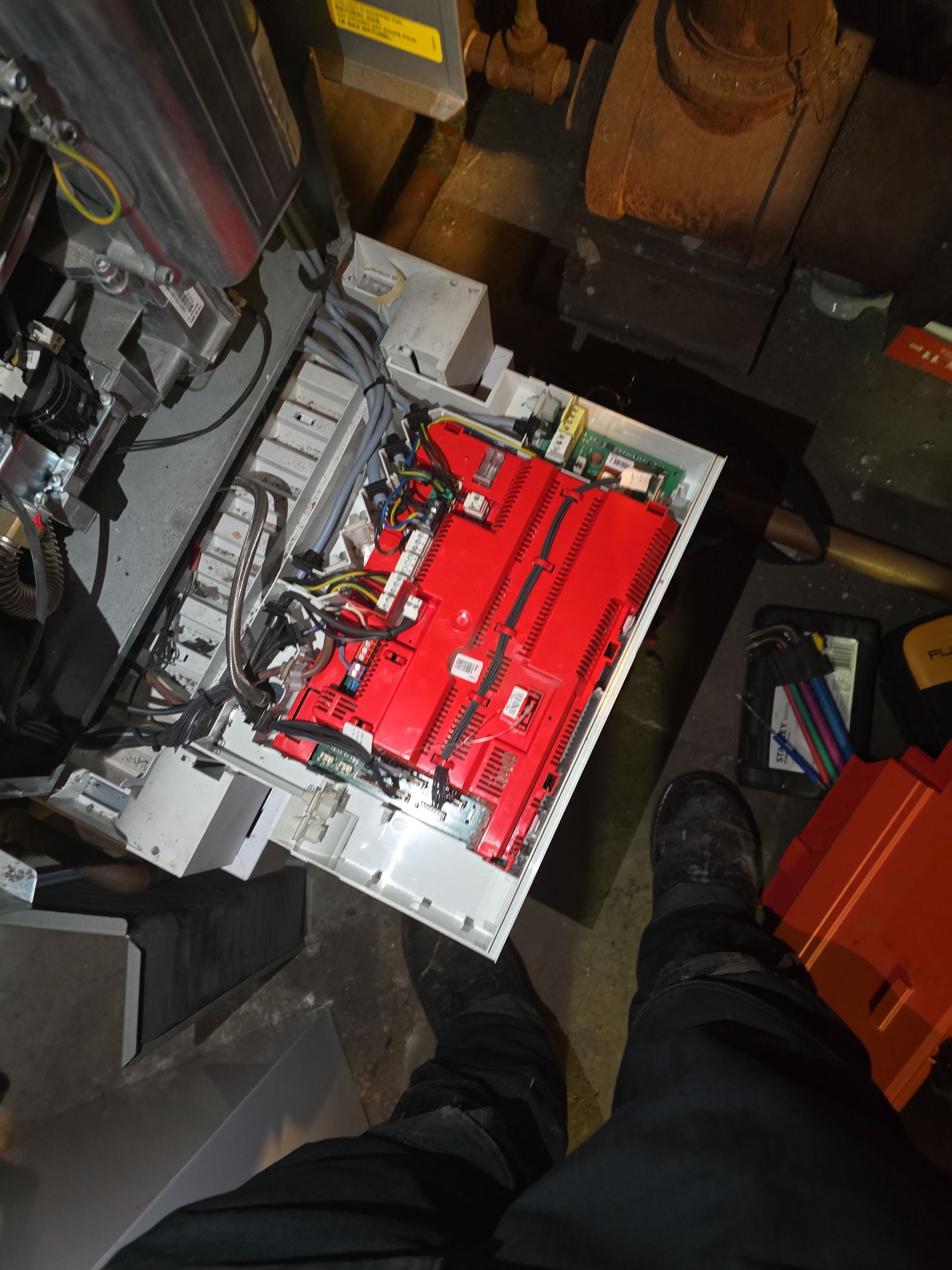 Person in a workshop inspecting the open insides of a red electronic device in a gray enclosure.