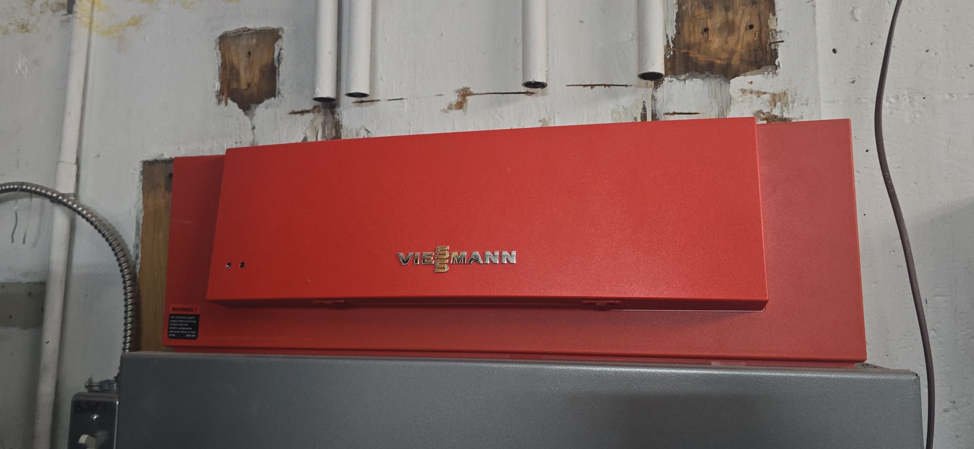 Red Viessmann furnace mounted on a gray unit against a wall with exposed pipes.