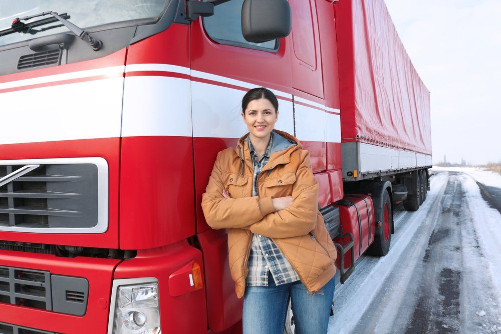 woman semi truck driver standing next to her truck on a snowy road
