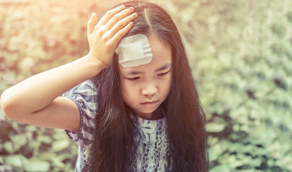 young girl holding her head with bandaid on forehead 
