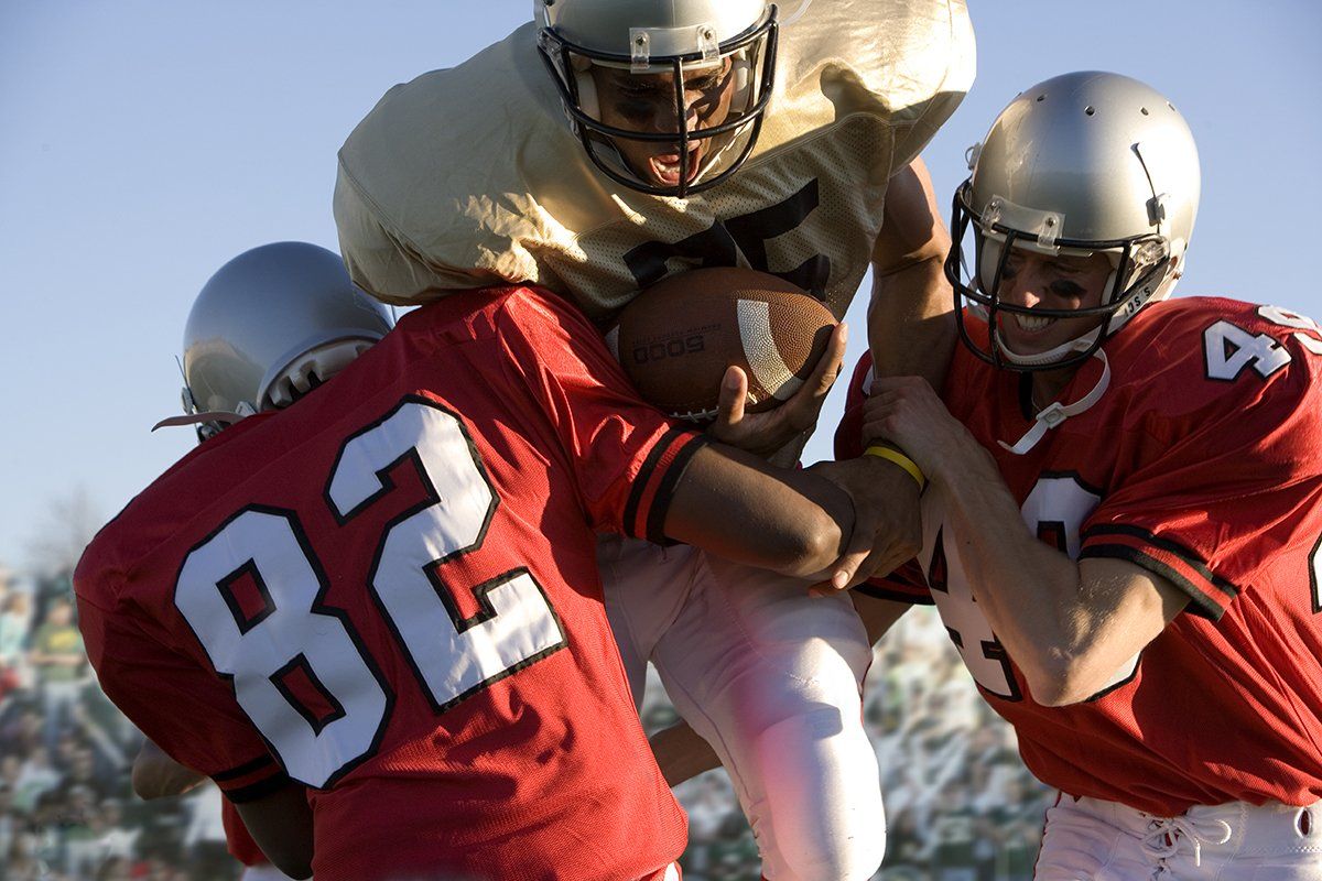 Football player is tackled by two others, which can cause catastrophic brain injury