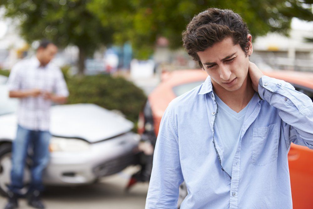 young man holding his neck from suffering whiplash during a car accident