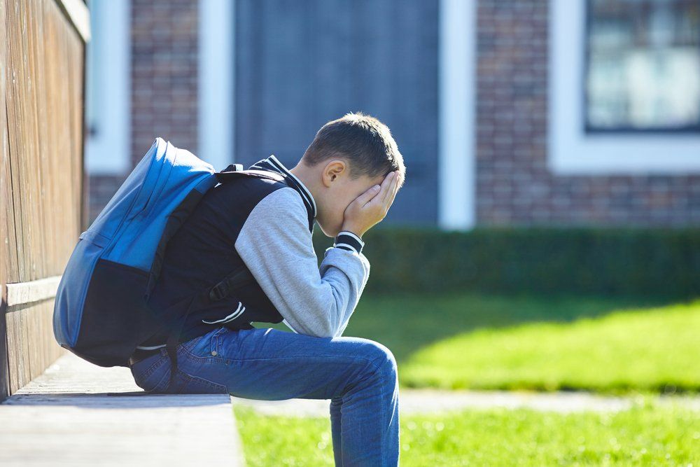 boy crying while sitting on a bench outside of school