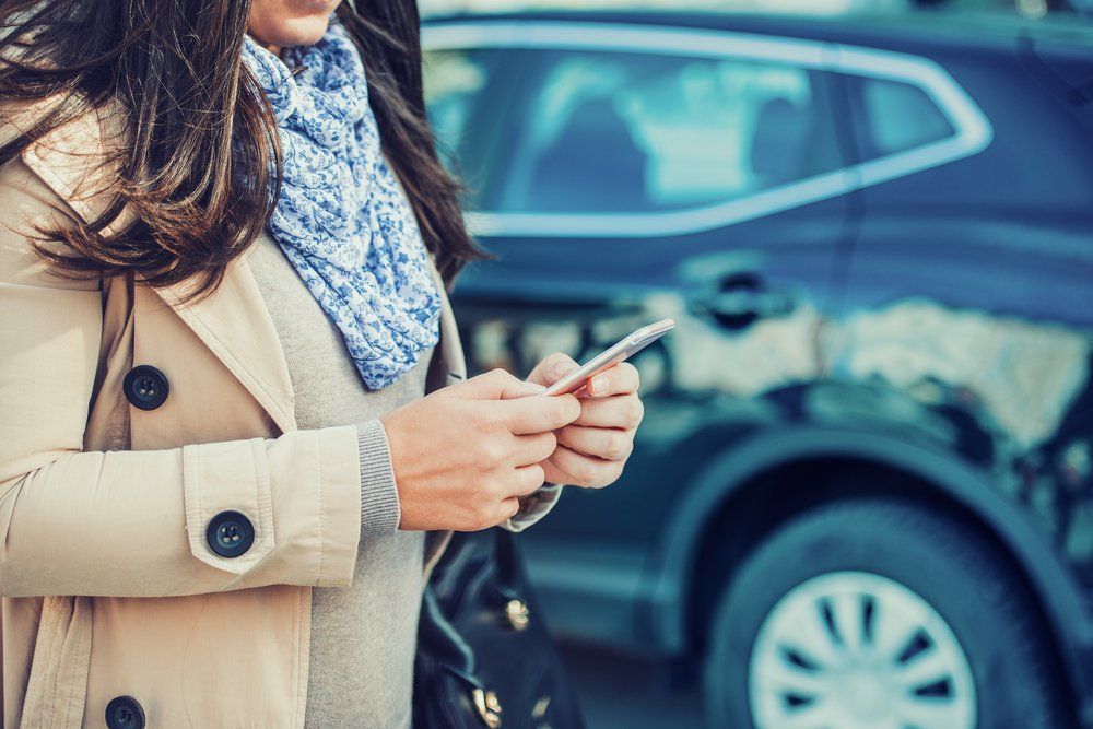 woman texting on a phone standing next to her car