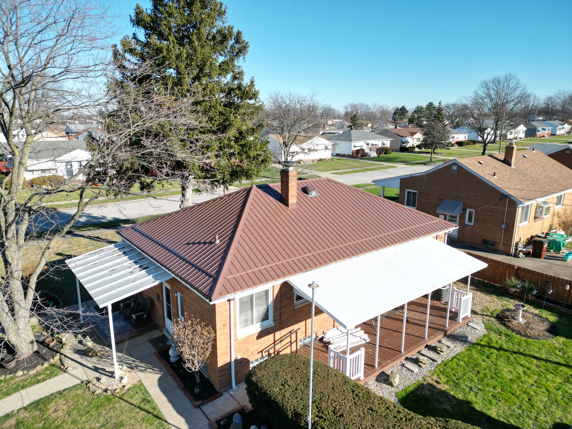 An aerial view of a brick house with a brown roof and attached awnings, in a residential neighborhood.