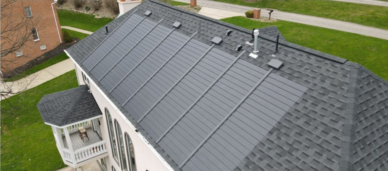 An aerial view of a house with dark solar panels installed on the roof. Green grass surrounds the house.