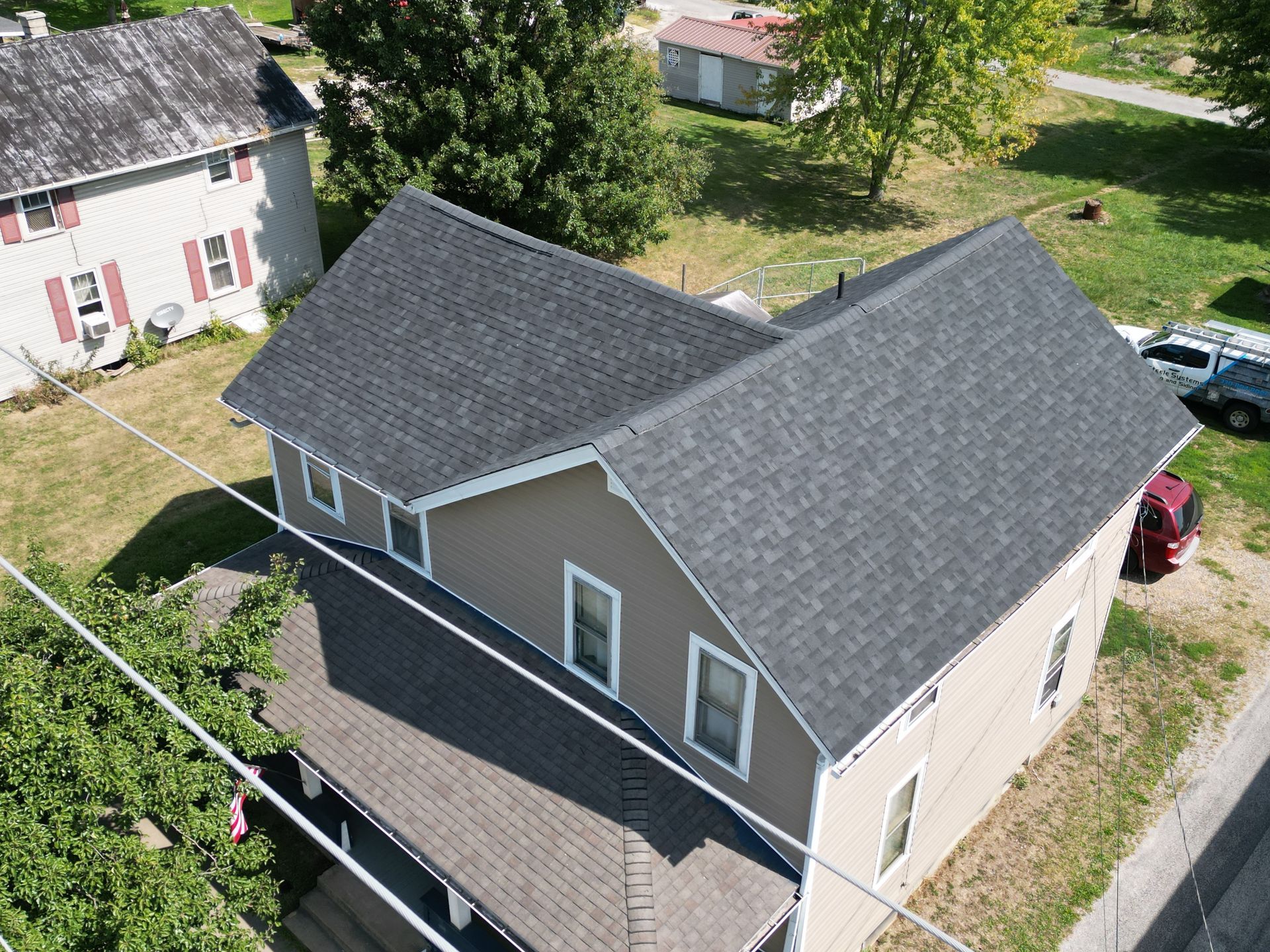 Aerial view of a two-story house with a dark gray roof and beige siding. A neighboring house and yard are visible.
