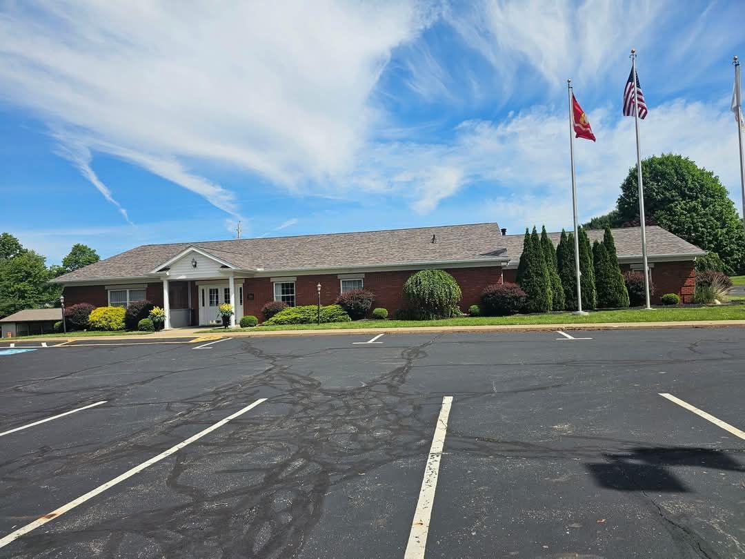 A brick building with a parking lot in front; several flags fly in the blue sky.