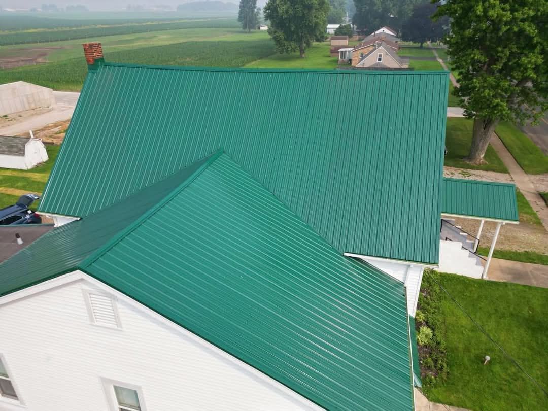 Green metal roof on a white house in a rural setting. The roof has a patterned design.