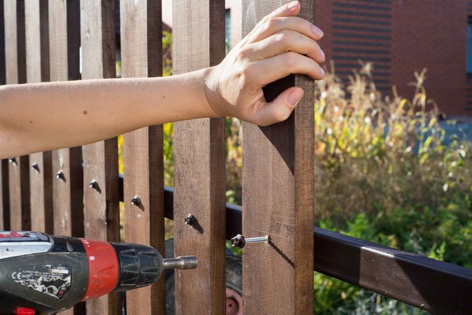 Worker screwing in wood picket to a fence rail