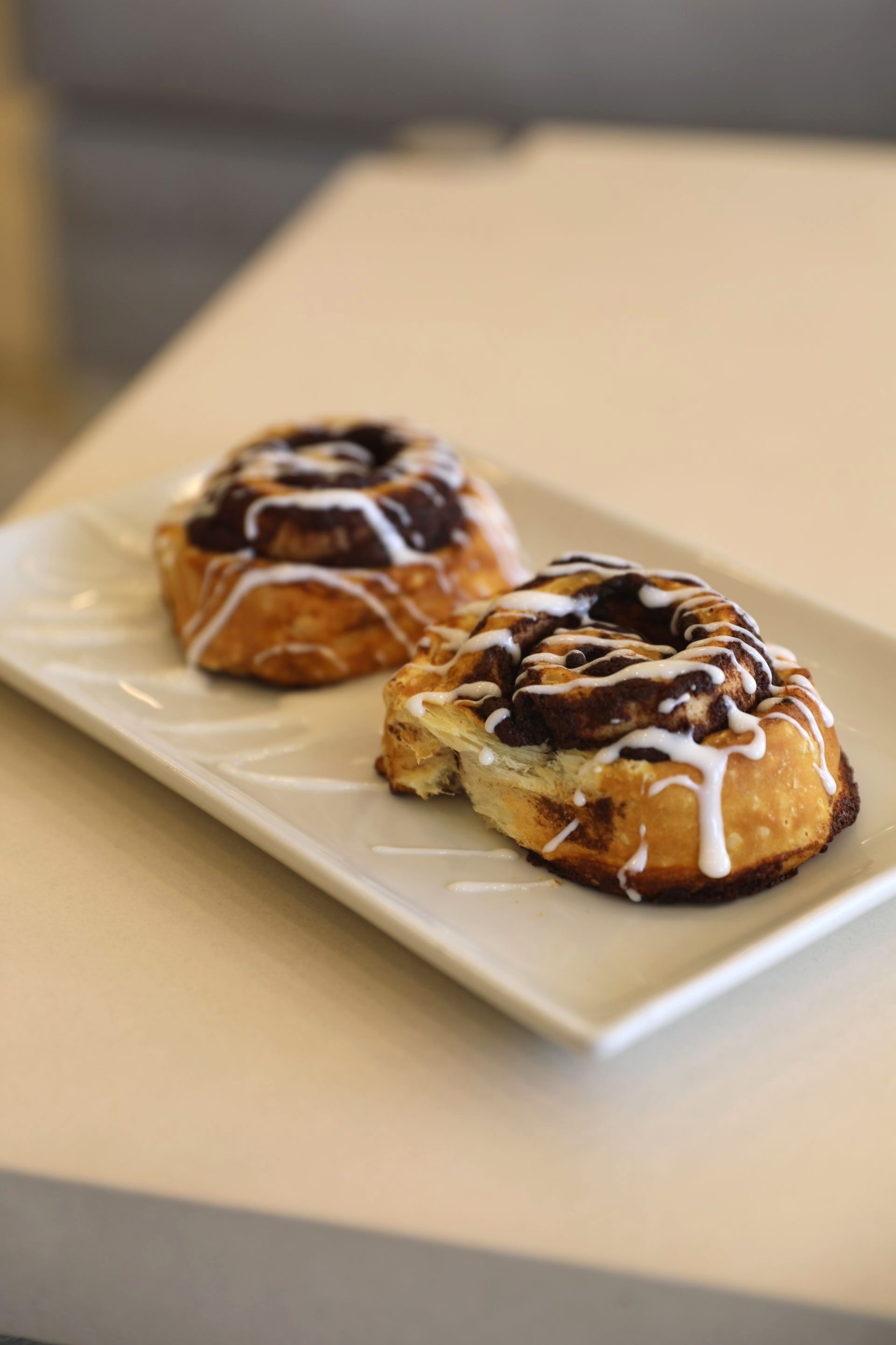 Two cinnamon rolls are on a white plate on a table.