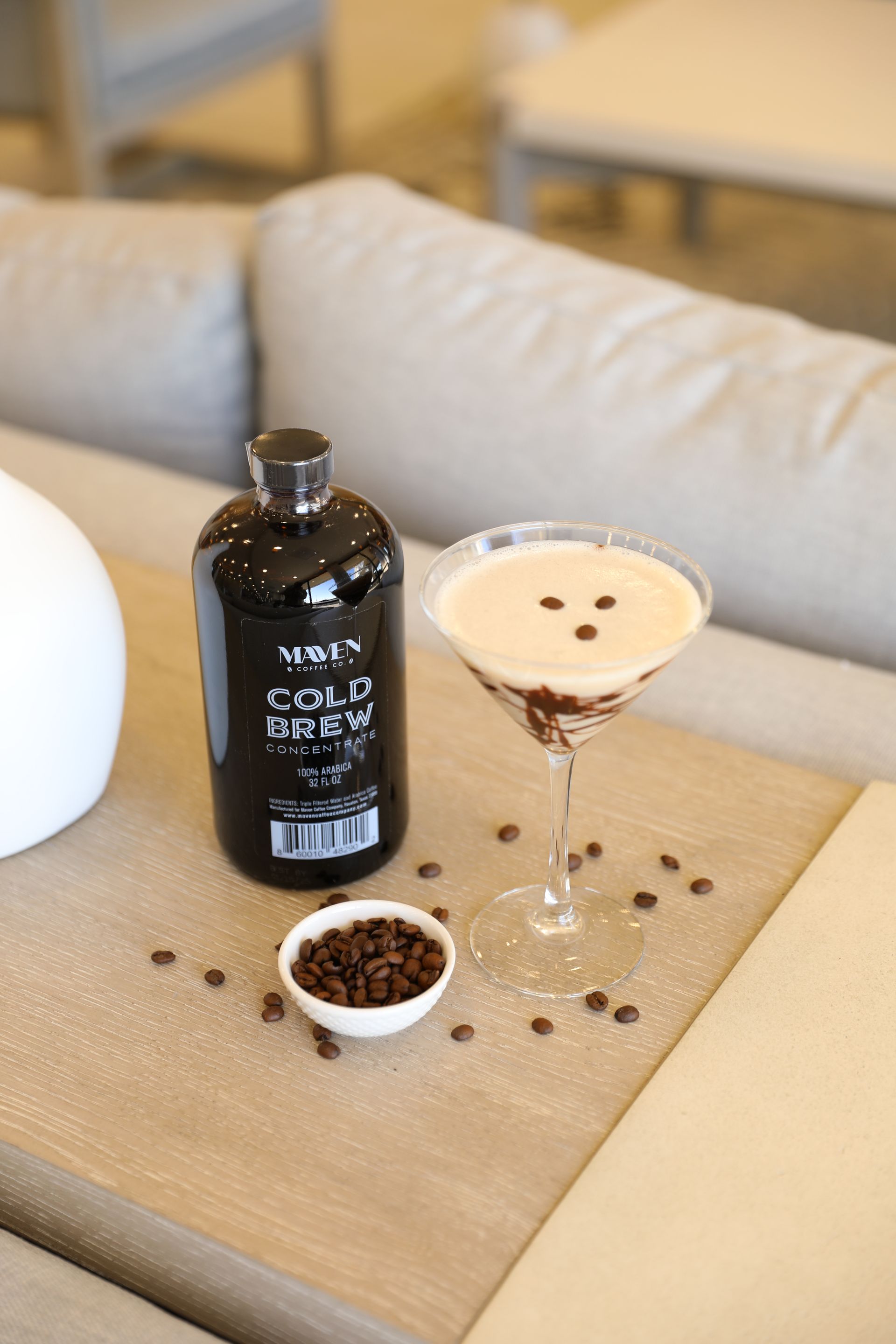 A bottle of coffee liqueur next to an espresso martini cocktail on a table.