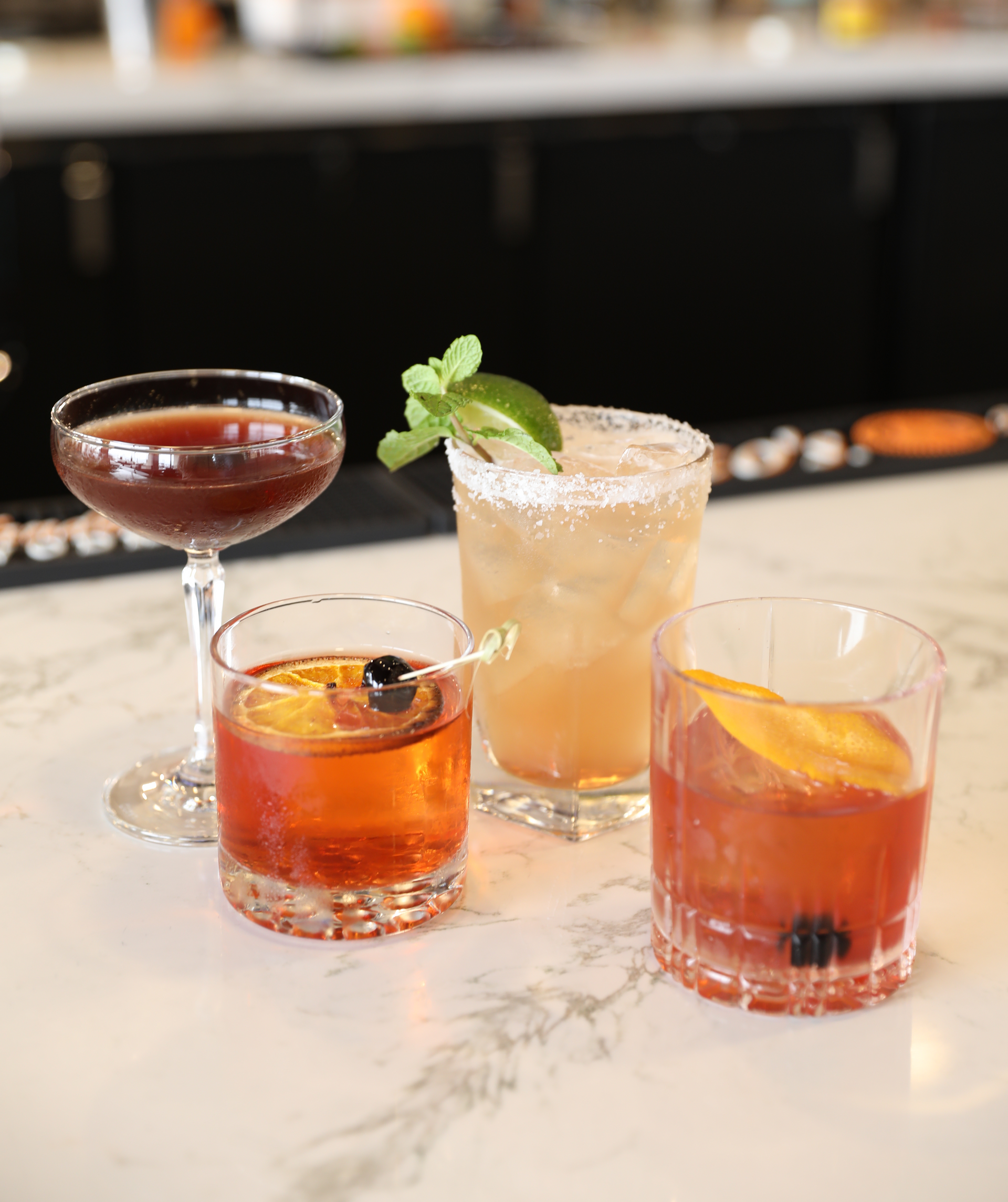 Four different types of cocktails are sitting on a bar counter.