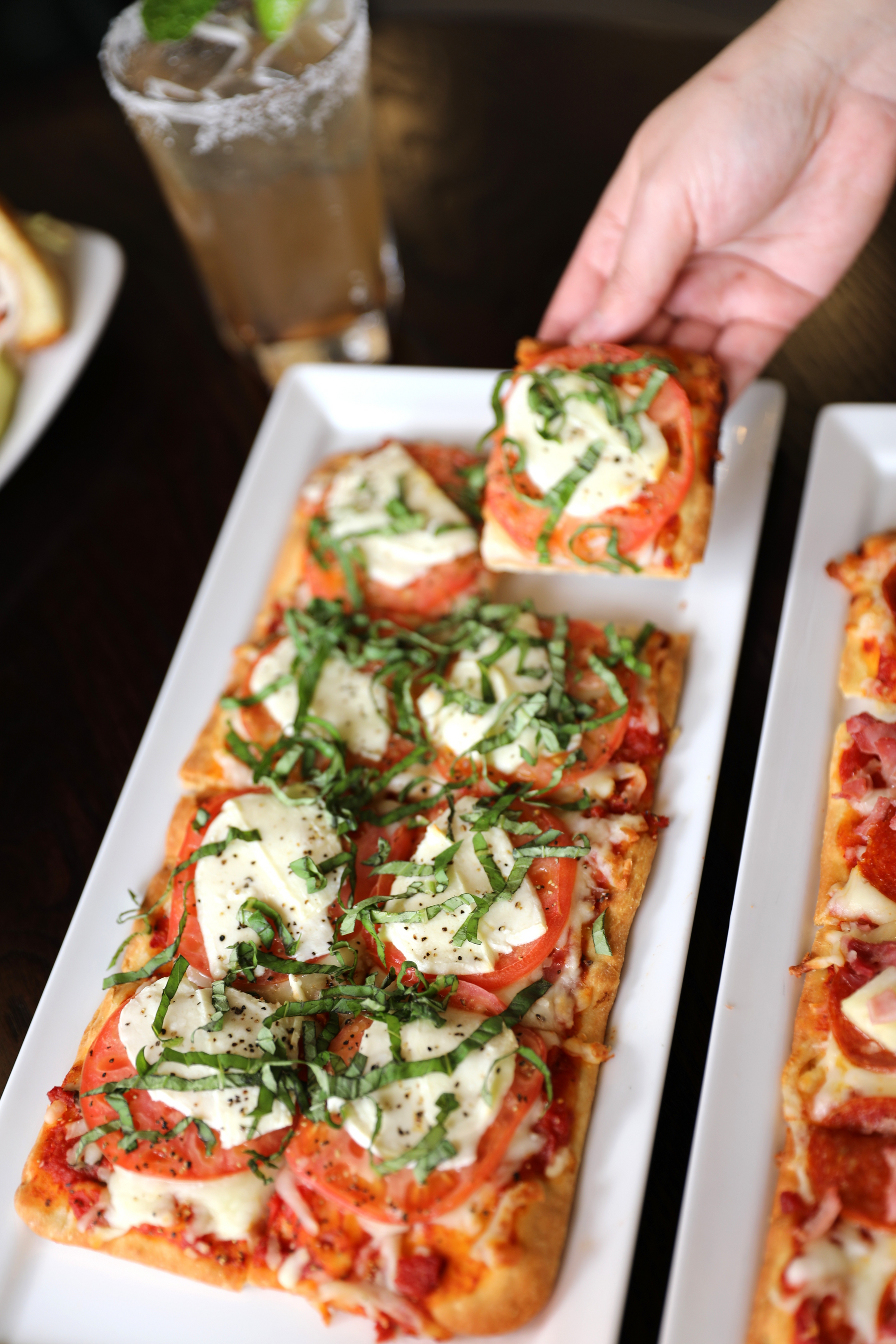 A person is taking a slice of pizza from a white plate.