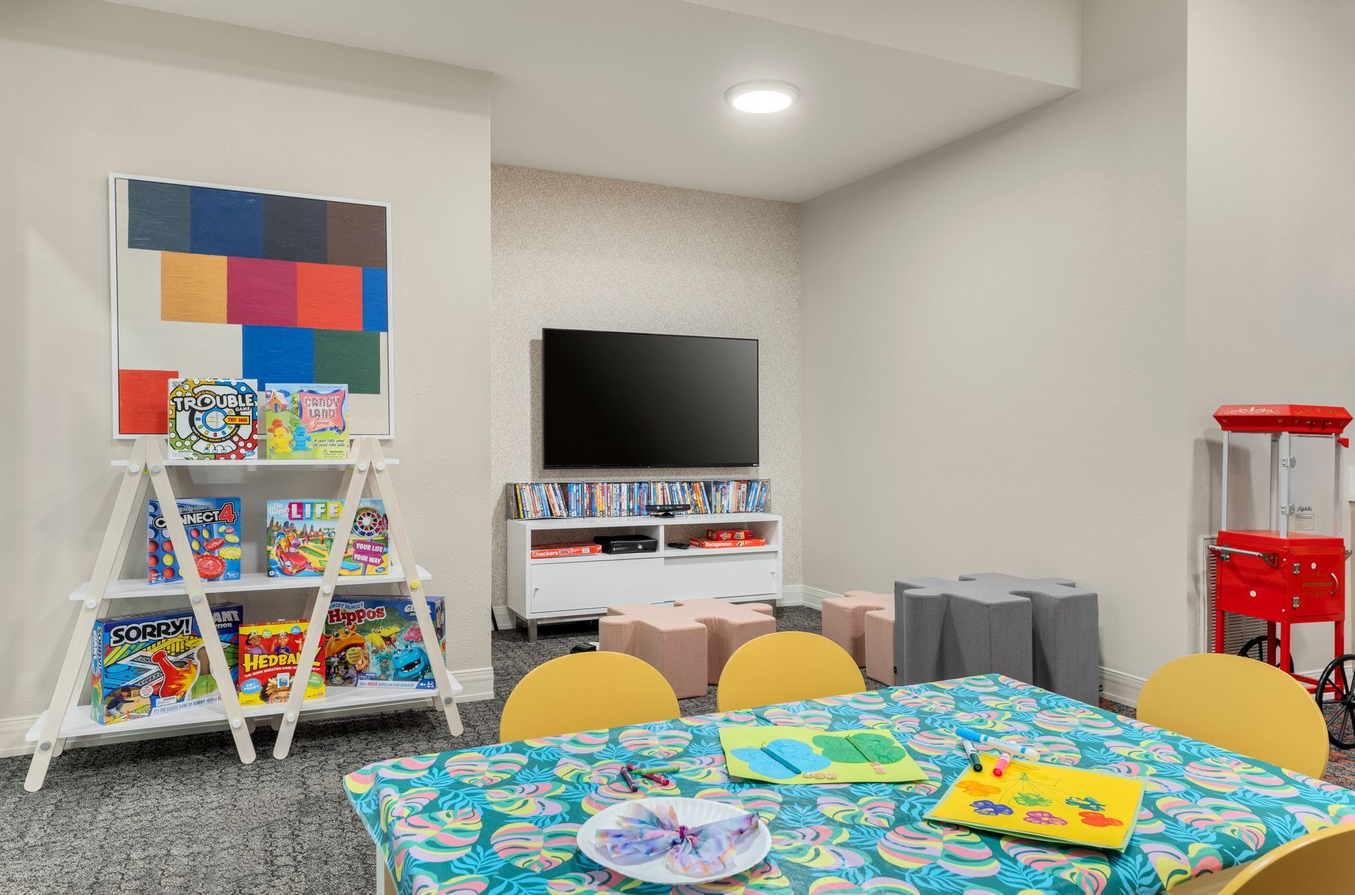A children's room with tables, chairs, arts and crafts supplies, games, and a television.