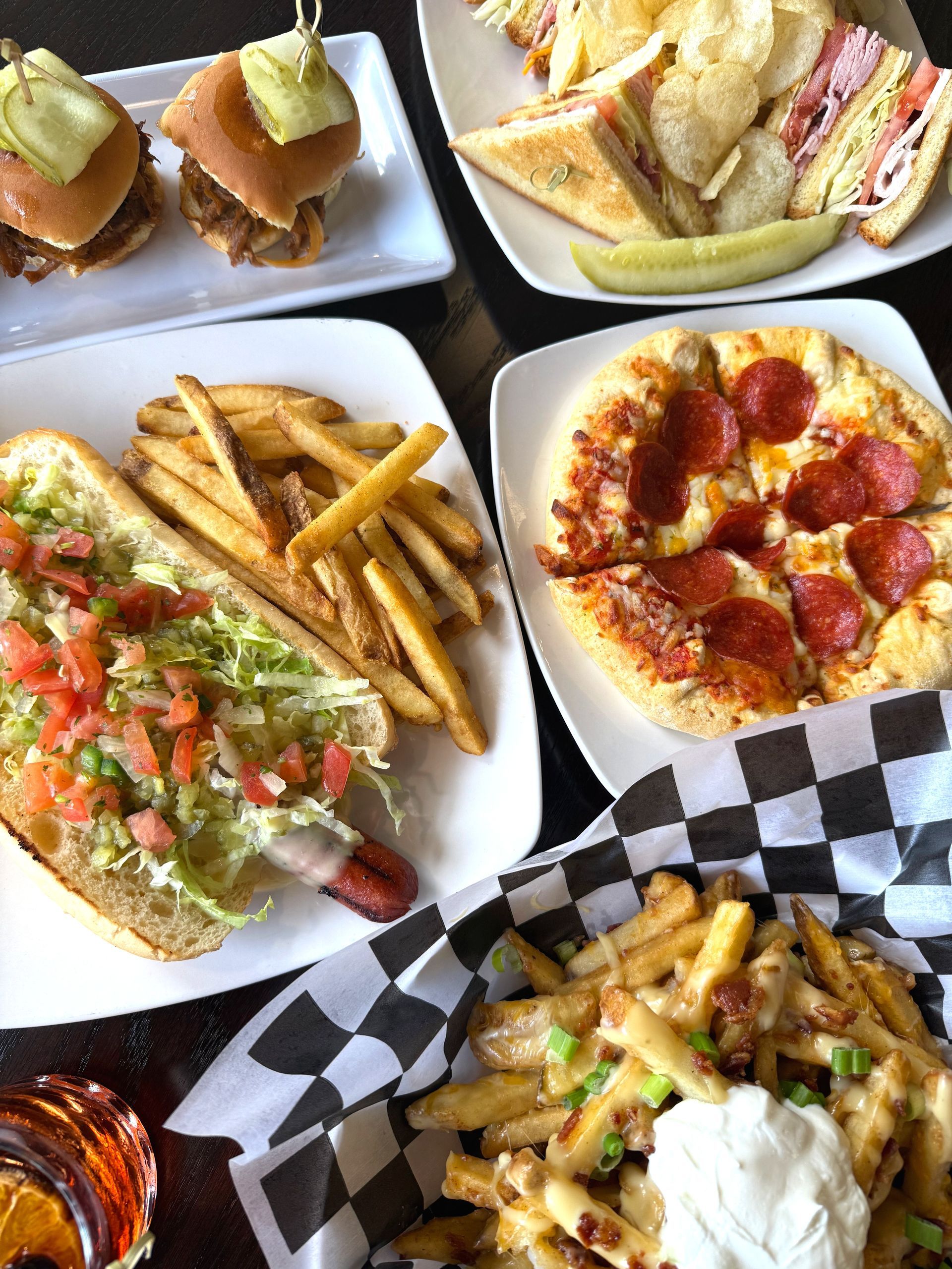 A table topped with plates of food including pizza, french fries, sandwiches, and a hot dog.