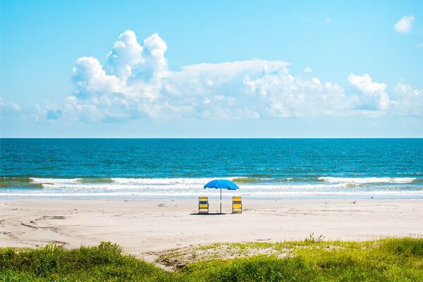There are two chairs and an umbrella on the beach.