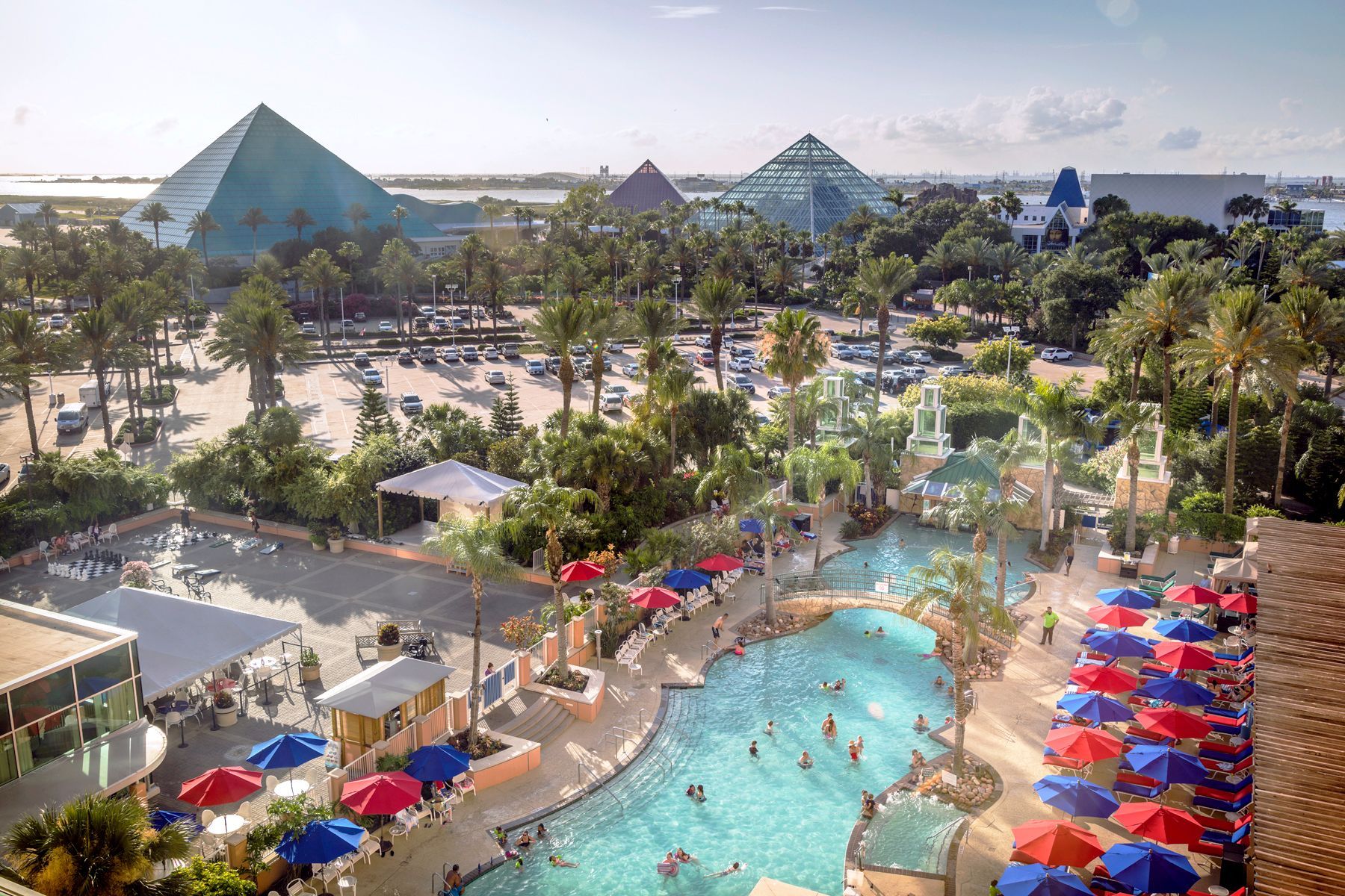 An aerial view of a large lazy river surrounded by umbrellas and palm trees.