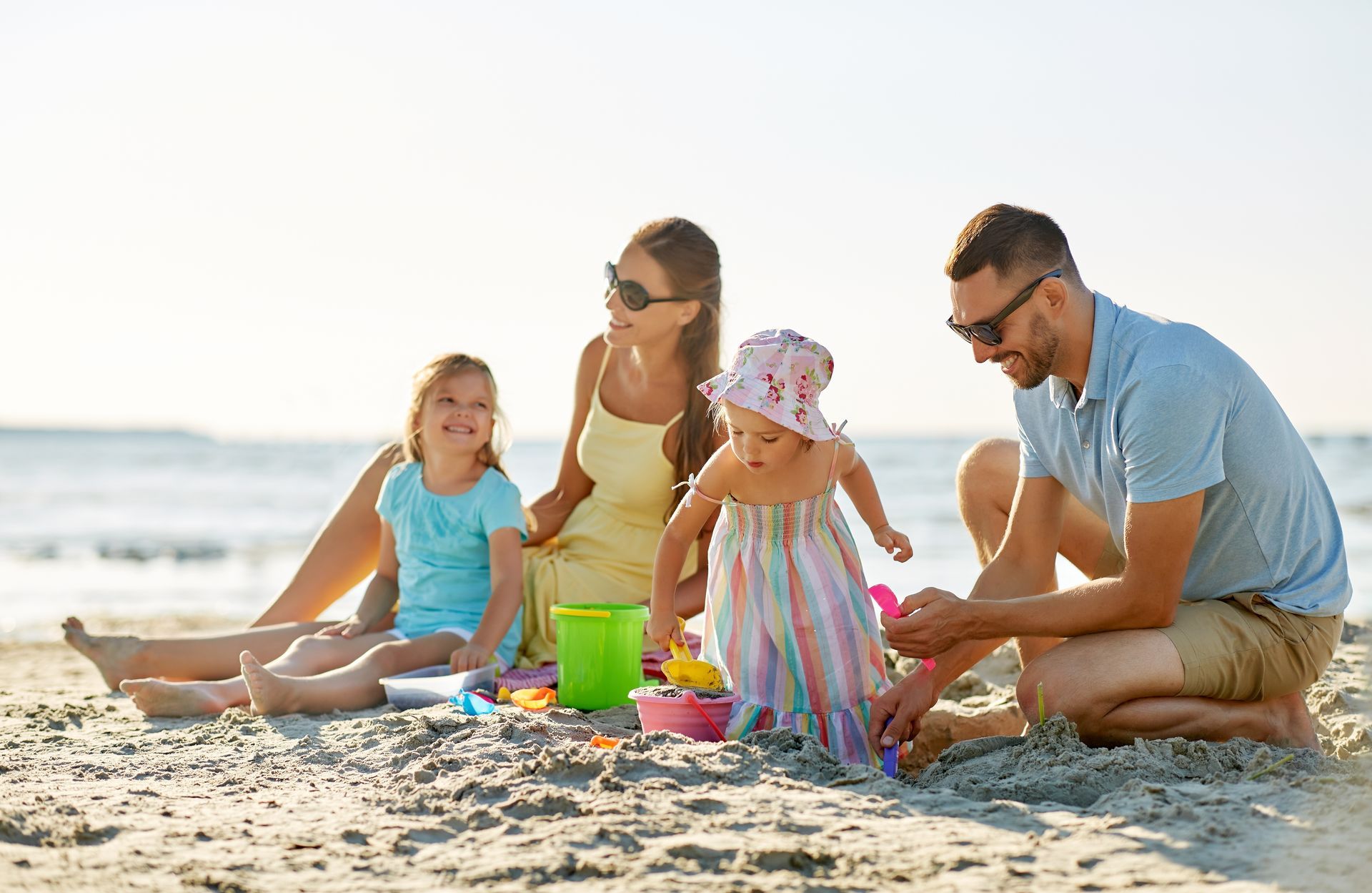 Parents are sitting on the beach playing in the sand with their two daughters.