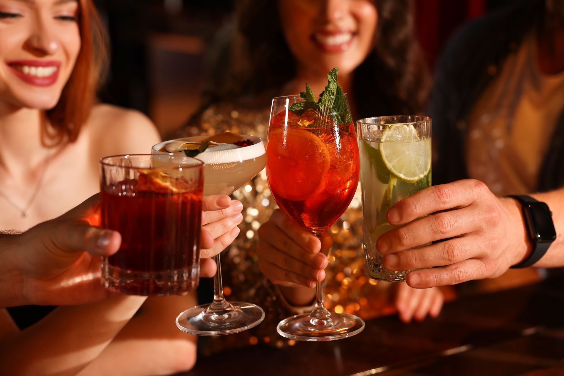Friends clinking colorful cocktails at a bar, smiling in warm evening light