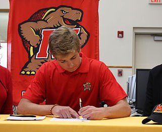 A man in a red shirt is sitting at a table signing a document.