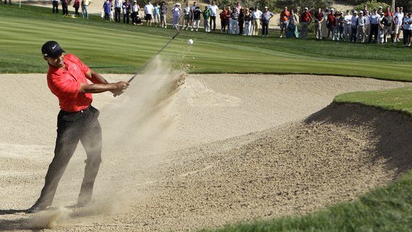A man is hitting a golf ball out of a bunker on a golf course.