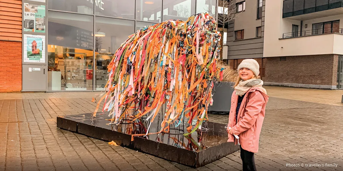 Un enfant devant une installation artistique composée de morceaux de papier colorés et représentant un mammouth.
