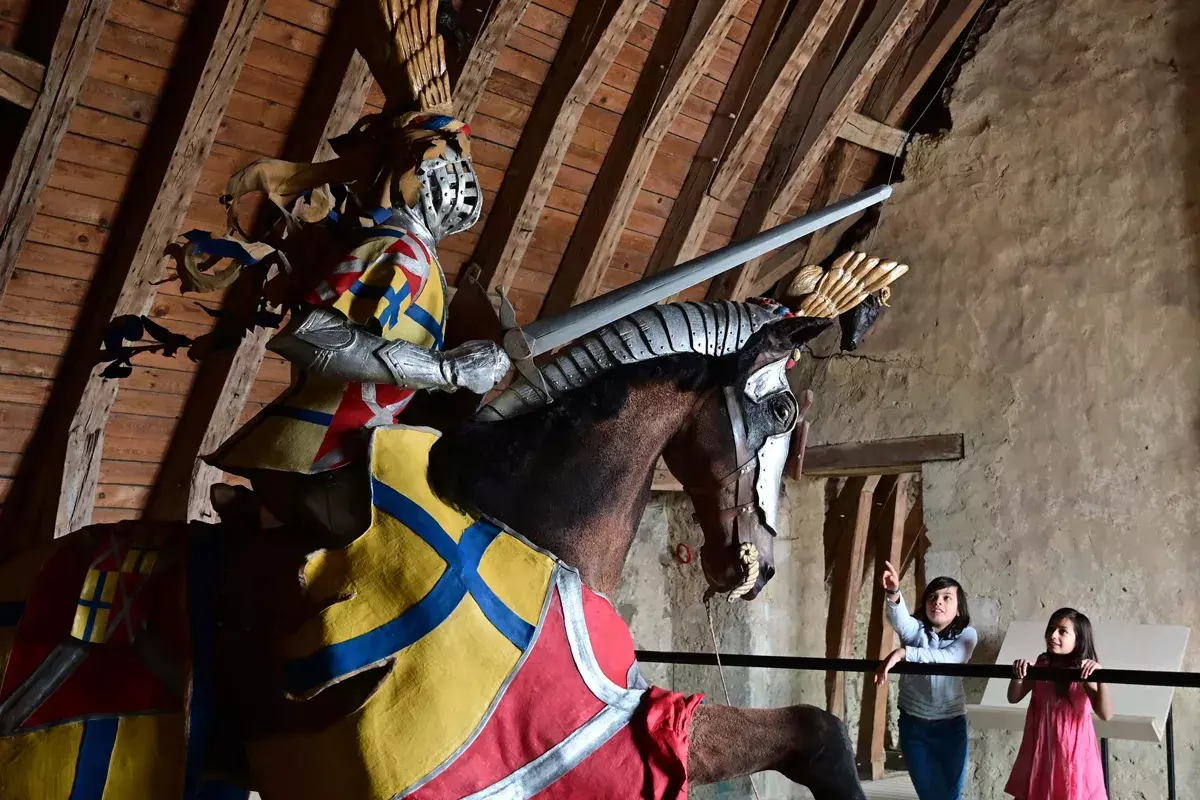 Deux enfants observent une réplique d’un chevalier en armure, sur un cheval, à l’intérieur du Château de Baugé.