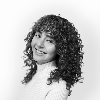 A woman with curly hair is smiling in a black and white photo.