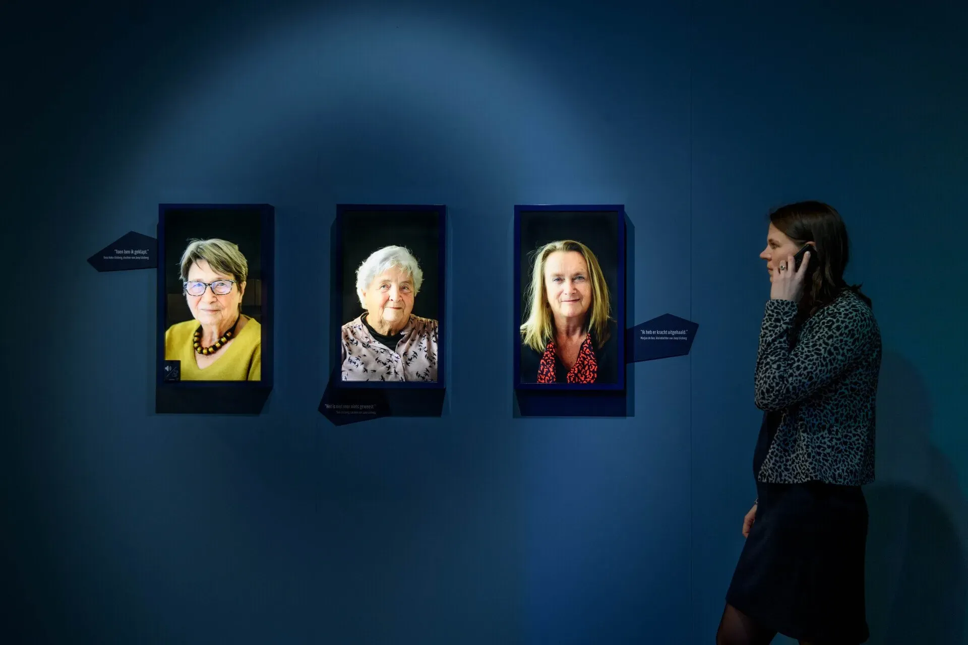 A person is listening to a Podcatcher in front of three photos of people at the Resistance Museum.